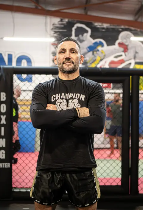 Un homme barbu se tient debout croisant les bras sur son torse. Coach du club Cage Fight Toulouse.